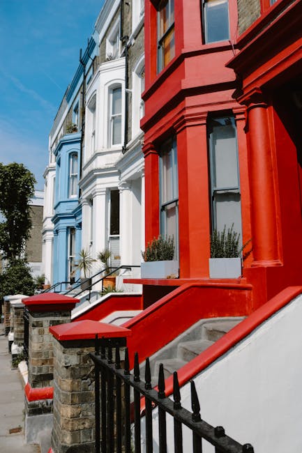 Close-up view of the exterior of a row of Victorian terraced houses in Notting Hill, London, featuring colorful facades painted in shades of blue, white, and red. The buildings have large sash windows
